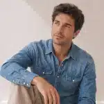 Man in a denim shirt with clear, healthy skin sitting relaxed, showcasing a natural, well-groomed complexion