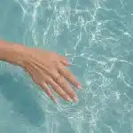 Close-up of a woman's hand with smooth, youthful skin trailing through clear turquoise water