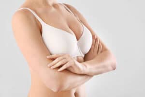 Woman with her arms folded in bra following cosmetic breast surgery.