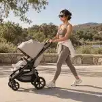 Woman in athletic wear walking a stroller along a sunlit lakeside path
