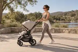 Woman in athletic wear walking a stroller along a sunlit lakeside path