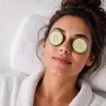 Woman in a white robe relaxing on a spa bed with cucumber slices over her eyes